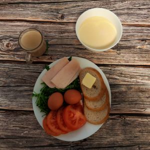 Zdjęcie przedstawia Dietę łatwostrawną: Kawa zbożowa z mlekiem kasza kukurydziana na mleku Bułka pszenna długa krojona Masło extra Szynka tostowa Jajko gotowane Pomidor Rukola Woda mineralna